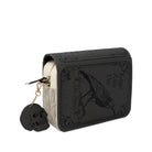 A black faux-leather book-style crossbody featuring embossed gothic artwork of a raven and the text 'Hester Allan Poe' from 'The Raven', with a cream-colored page edge visible on the left and a dangling black skull charm on a gold chain.