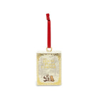 A decorative Christmas ornament shaped like a vintage book cover featuring a red hanging ribbon and gold ornamental border details on a white background.