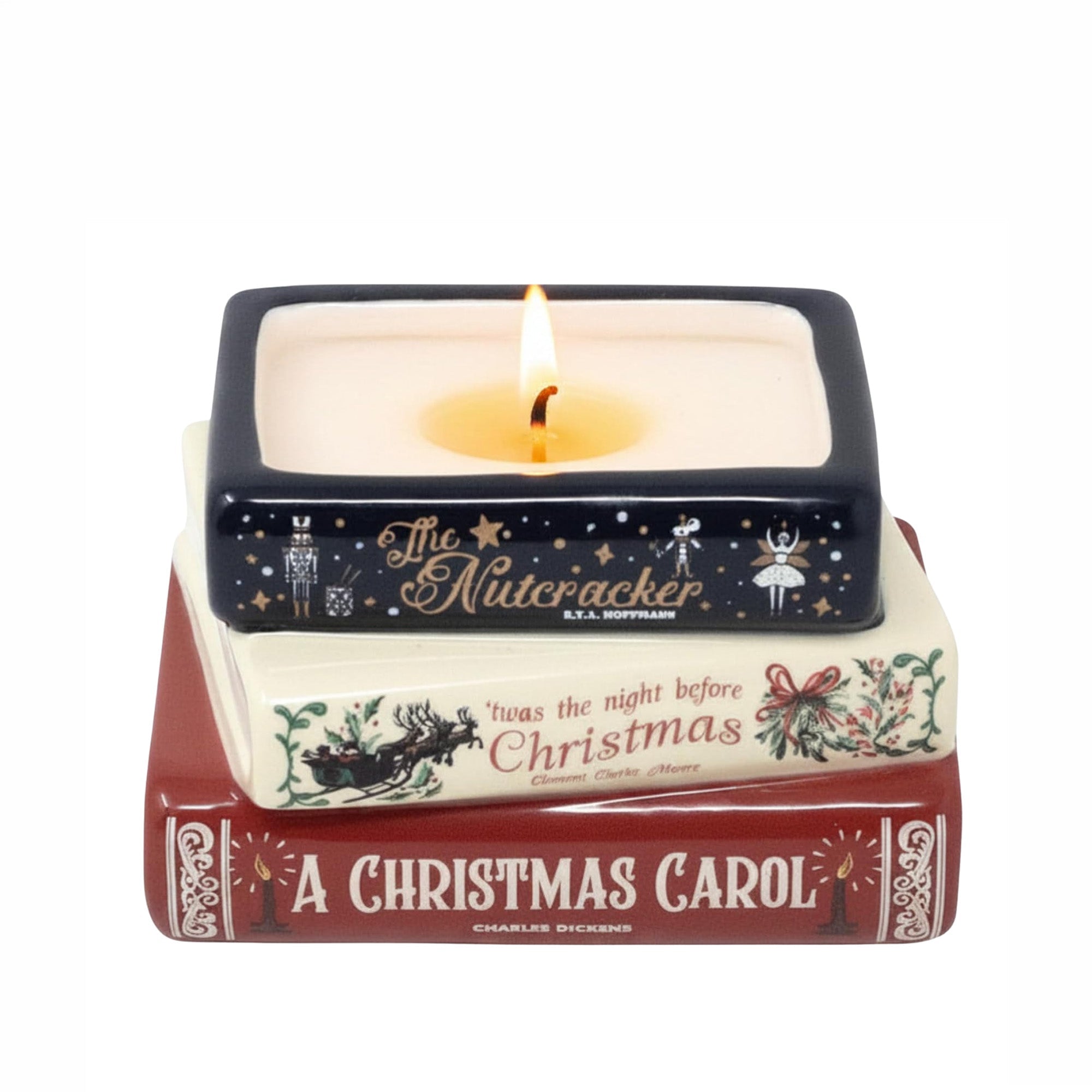 A square ceramic candle holder styled like a stack of Christmas books, with a lit candle inside. The top book is dark navy blue with gold Nutcracker illustrations and text; the middle book is cream with red and green holiday text and illustrations; the bottom book is dark red with white text reading 'A Christmas Carol.'