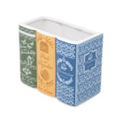 A rectangular ceramic container designed to look like three vintage book spines, featuring green, orange, and blue patterns with decorative text and illustrations.