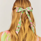 Floral hair bow in green and pink on a person with long blonde hair against a white background