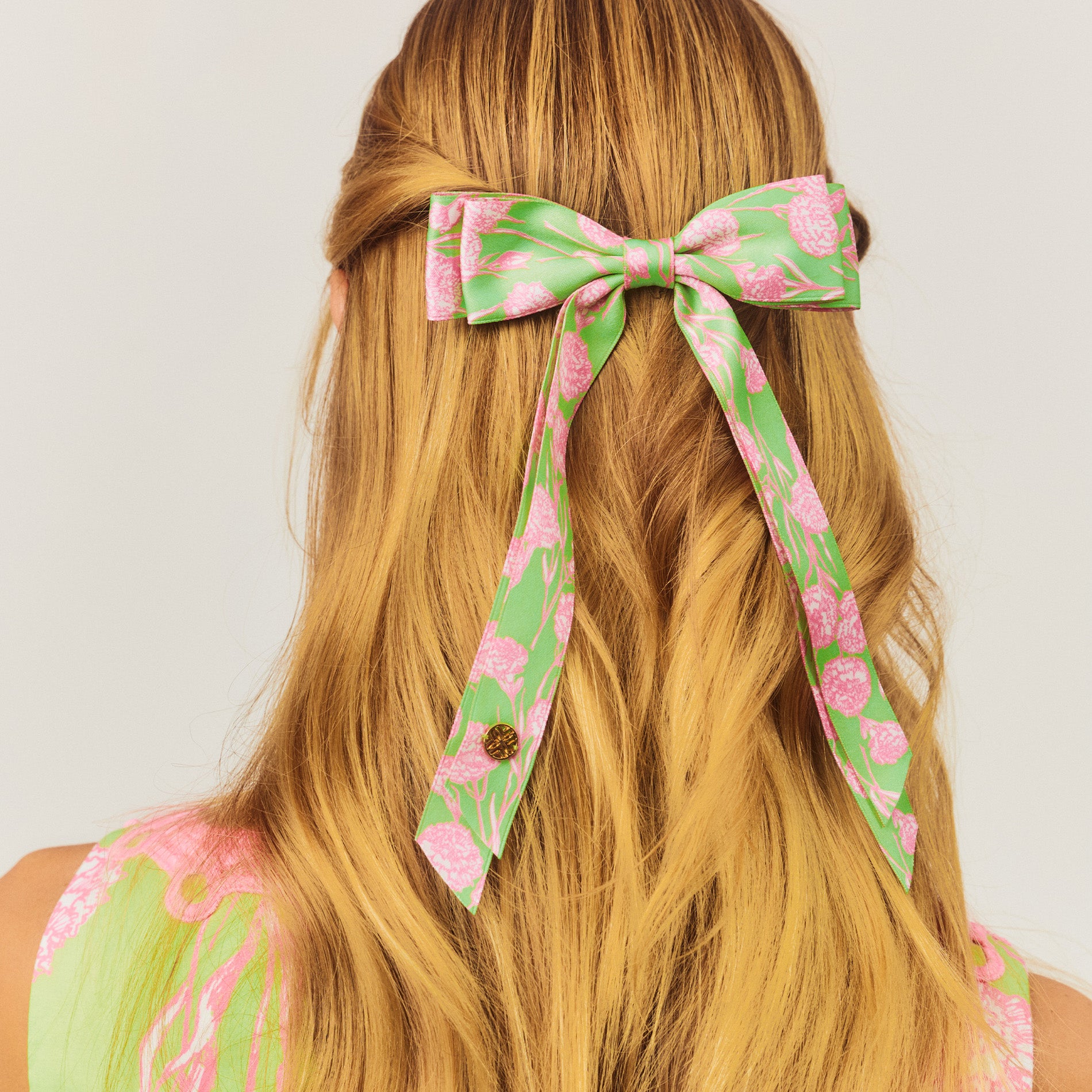 Floral hair bow in green and pink on a person with long blonde hair against a white background
