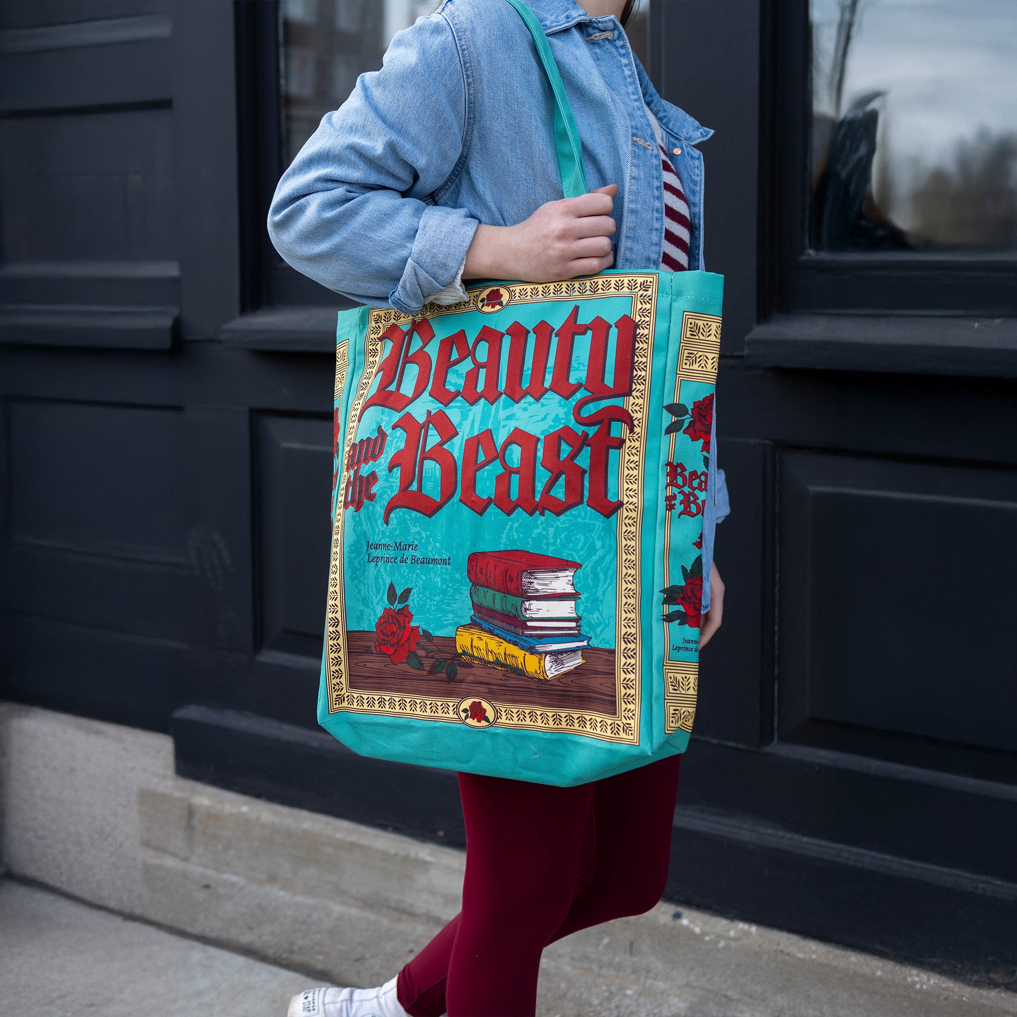Person holding a 'Beauty and the Beast' themed tote bag in front of a dark door.