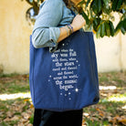 model carrying navy tote that says 'AND WHEN THE SKY WAS FULL WITH THEM, WHEN THE STARS RACES AND DANCED AND FLOWERS ACROSS THE WORLD, THE MUSIC BEGAN'