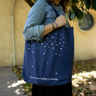 model carrying navy tote bag with star pattern and 'I'D NEVER SEEN ANYTHING SO BEAUTIFUL'