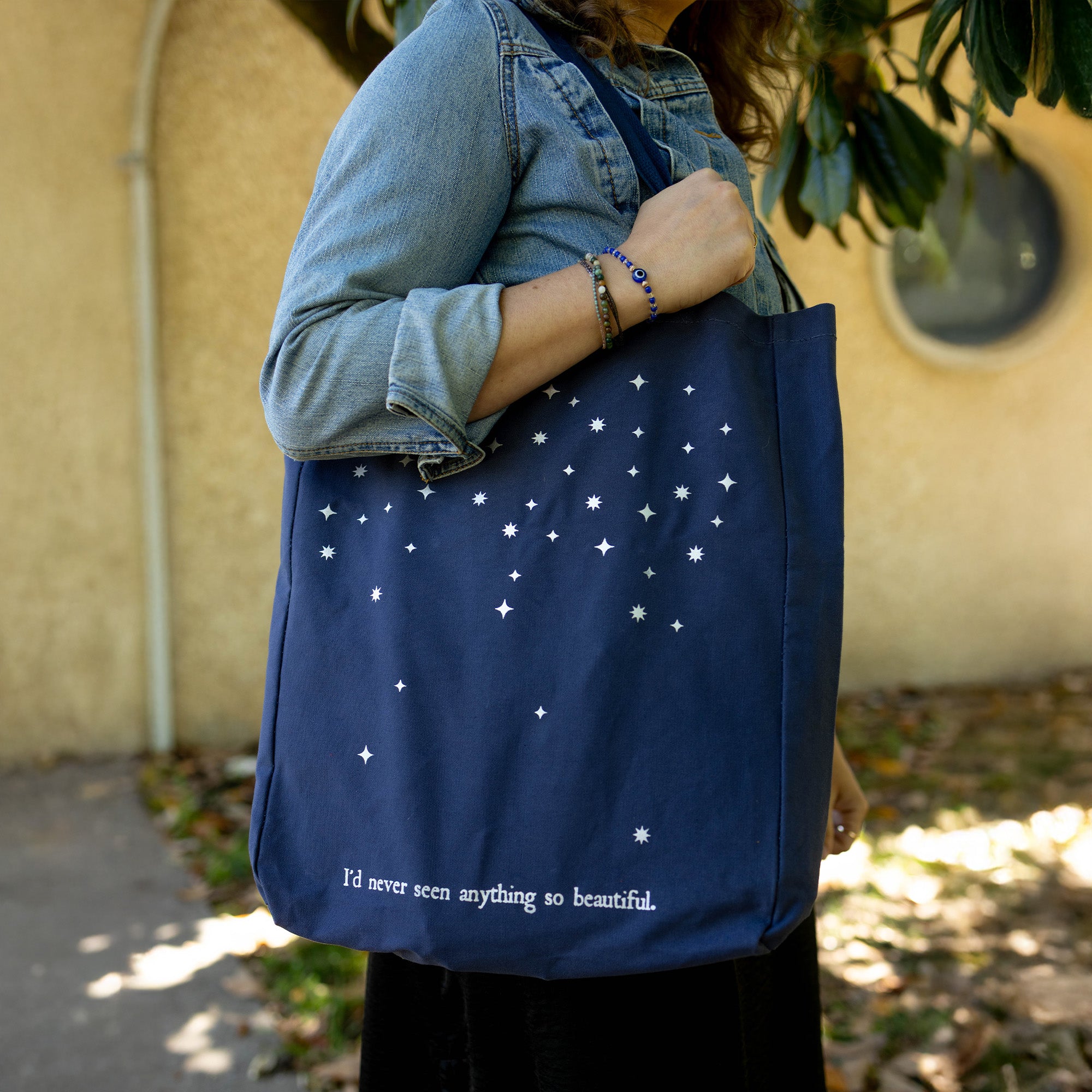 model carrying navy tote bag with star pattern and 'I'D NEVER SEEN ANYTHING SO BEAUTIFUL'