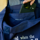 Person holding a phone over a blue tote with 'Sarah J. Maas' branding.