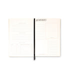 An open cream-colored spiral-bound planner or journal with lined pages, featuring a black elastic closure band and the word 'MEMORIES' printed at the top of one page, shown on a plain white background.