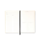 An open cream-colored daily planner or notebook with lined and blank writing sections on the left and right pages, held together by a black ribbon bookmark, shown on a plain white background.