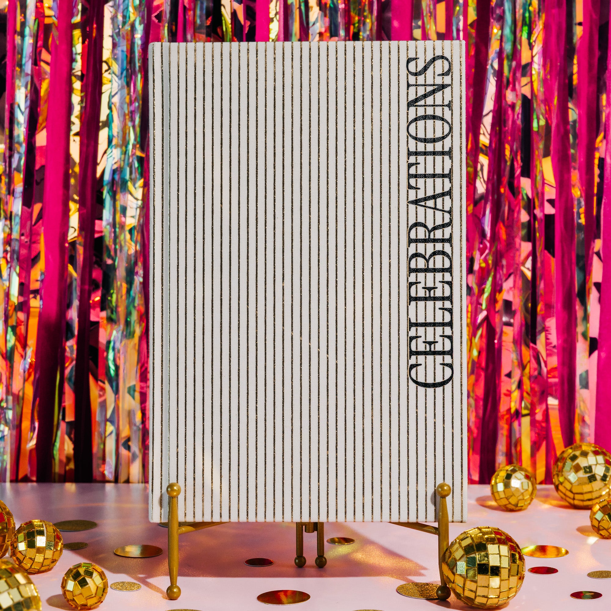 A vertical hardcover notebook with a cream-colored cover featuring thin vertical tan stripes and the word 'CELEBRATIONS' printed in black serif font along the right side, shown on a plain white background.