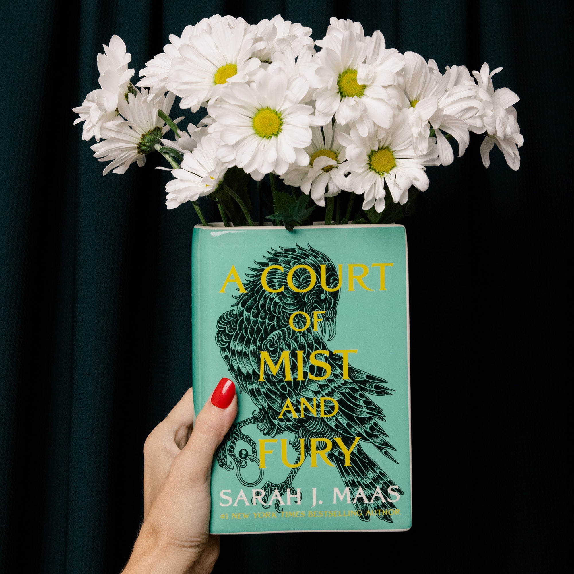 model holding 'A Court of Mist and Fury' by Sarah J. Maas vase with a green cover and white spine and white flowers inside