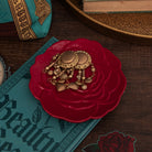 Gold jewelry on a red rose-shaped dish with a book and decorative items in the background