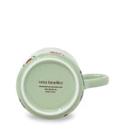 A light green ceramic mug shown from its bottom side, featuring the 'vera bradley' brand name printed in brown on the base. The mug has a pale green handle and a subtle floral pattern visible near the rim, set against a clean white background.
