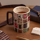 A ceramic mug filled with tea sits on a wooden table, decorated with a patchwork of vintage postage stamp designs in muted red, green, blue, and brown tones. The mug has a dark brown handle and the inside rim is printed with the text 'From Pembrory, with love'.