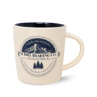 Beige mug with mountain and tree design and 'Suriel Trading Co.' text on a white background