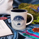 Beige mug with mountain and tree design and 'Suriel Trading Co.' text 