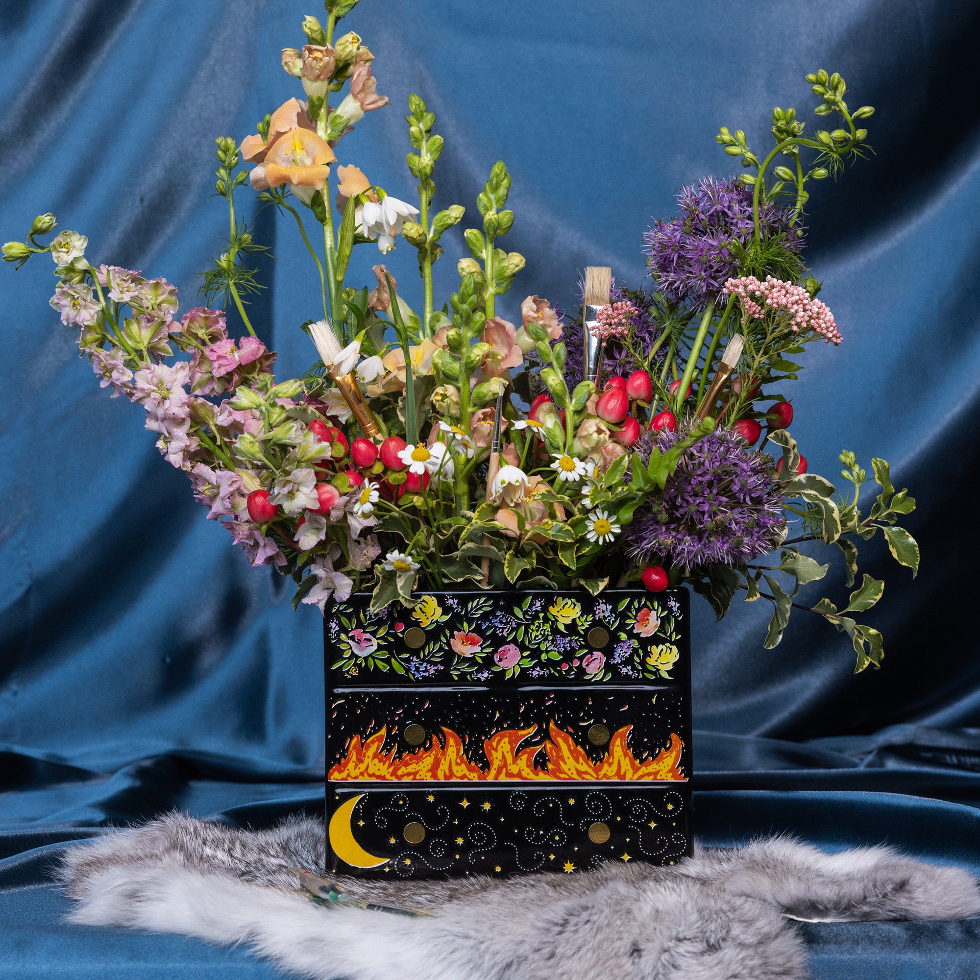 Black planter with floral and fiery designs with a bouquet inside