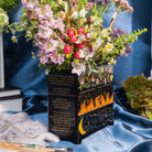side view of Black planter with floral and fiery designs with a bouquet inside