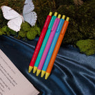 Five colorful pens with yellow tips on moss and a silky navy backdrop