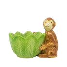 A green leaf-shaped ceramic bowl sits beside a small orange-brown monkey figurine