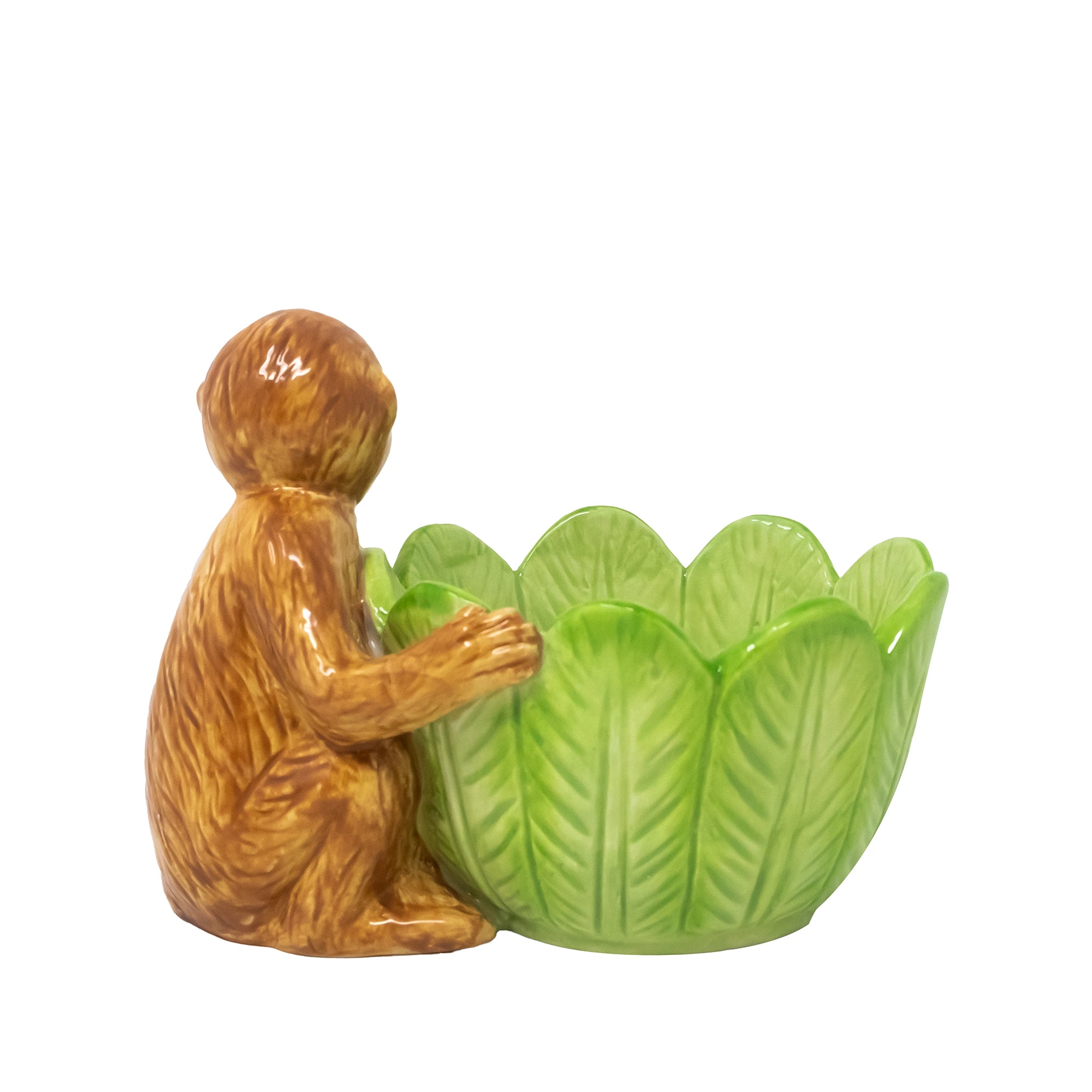 back view of a green leaf-shaped ceramic bowl sits beside a small orange-brown monkey figurine