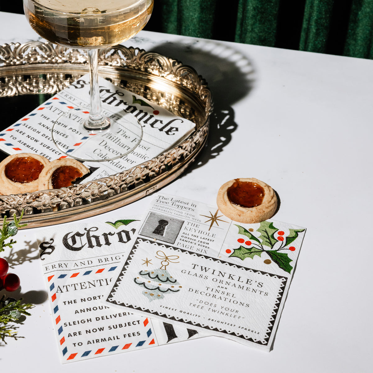 square paper napkins from The Christmas Chronicle, featuring vintage holiday illustrations, text snippets, and festive designs on a white table surrounded by holiday items