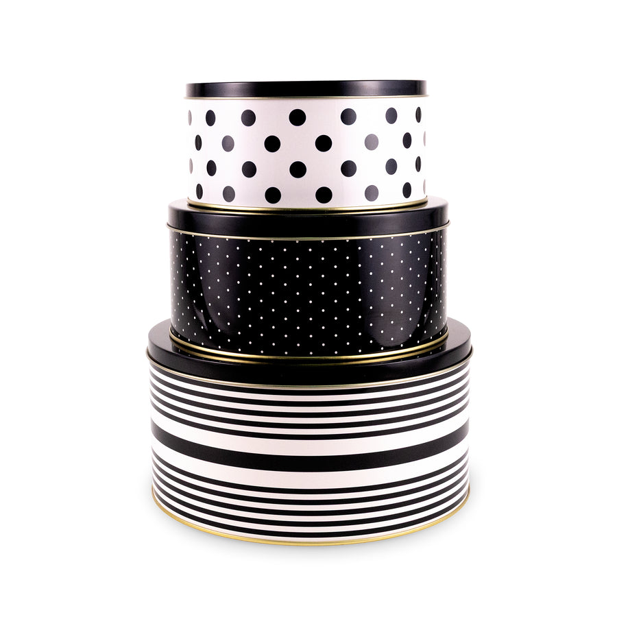 Three stacked round gift tins with black and white patterns, featuring polka dots and stripes, with thin gold trim, on a white background.