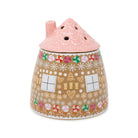 A ceramic gingerbread house-shaped vase with a pink scalloped roof and a decorated body featuring gingerbread cookies, candy canes, snowflakes, and windows on a white background.