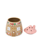 A gingerbread house-shaped ceramic vase with a pink lid, shown on a plain white background. The candle holder features a tan base decorated with white snowflakes, colorful flowers, and a brown door, while the lid beside it is light pink with a scalloped texture and small ventilation holes.
