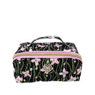 A rectangular zippered cosmetic bag with a black background and a pink, green, and white floral vine pattern. It features a top handle, a gold zipper, and a circular metal logo clasp on the front.