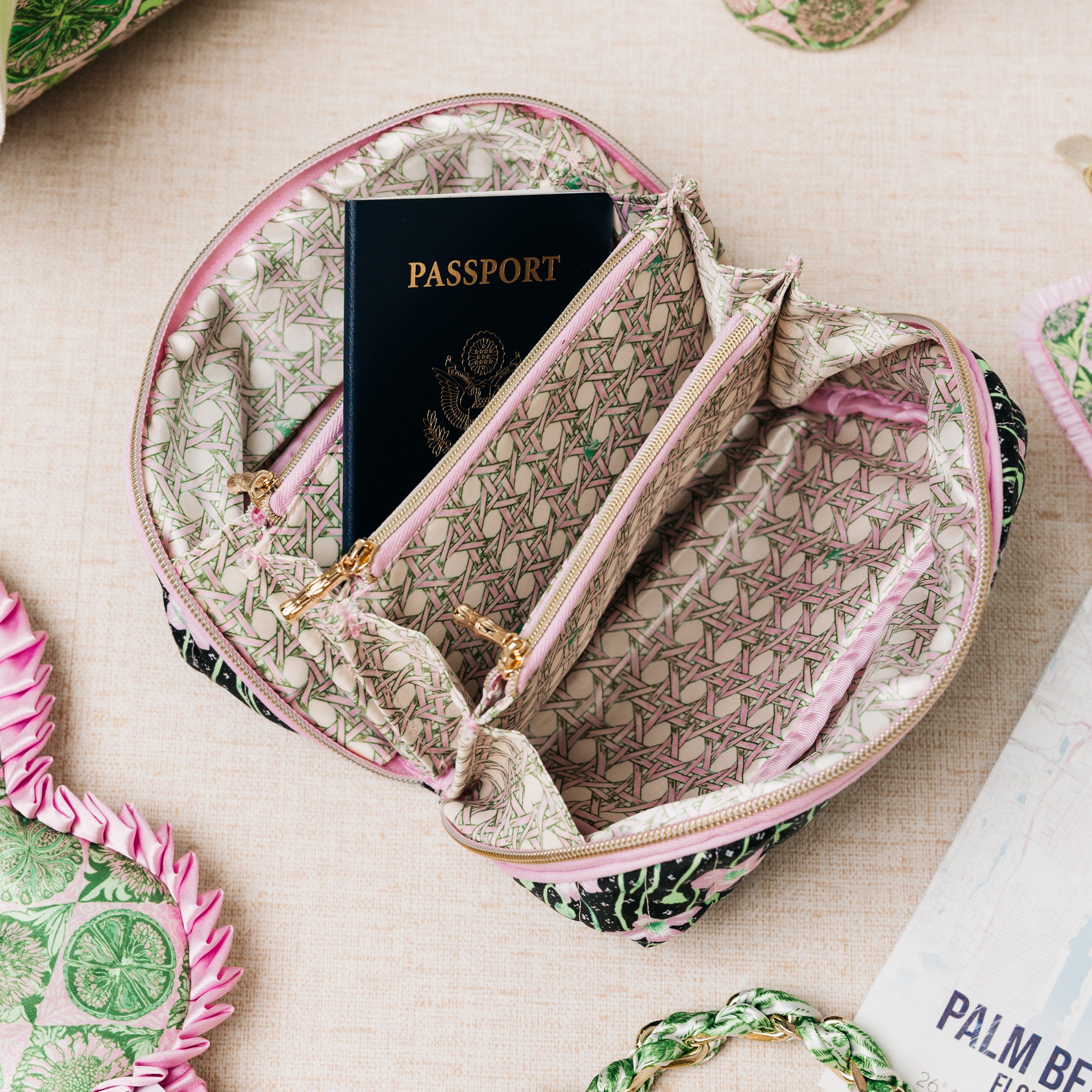 A zippered travel pouch with a geometric patterned fabric lining and a black patterned exterior, shown open with a passport inside. The pouch is photographed on a light beige textured surface with other travel accessories partially visible around it.