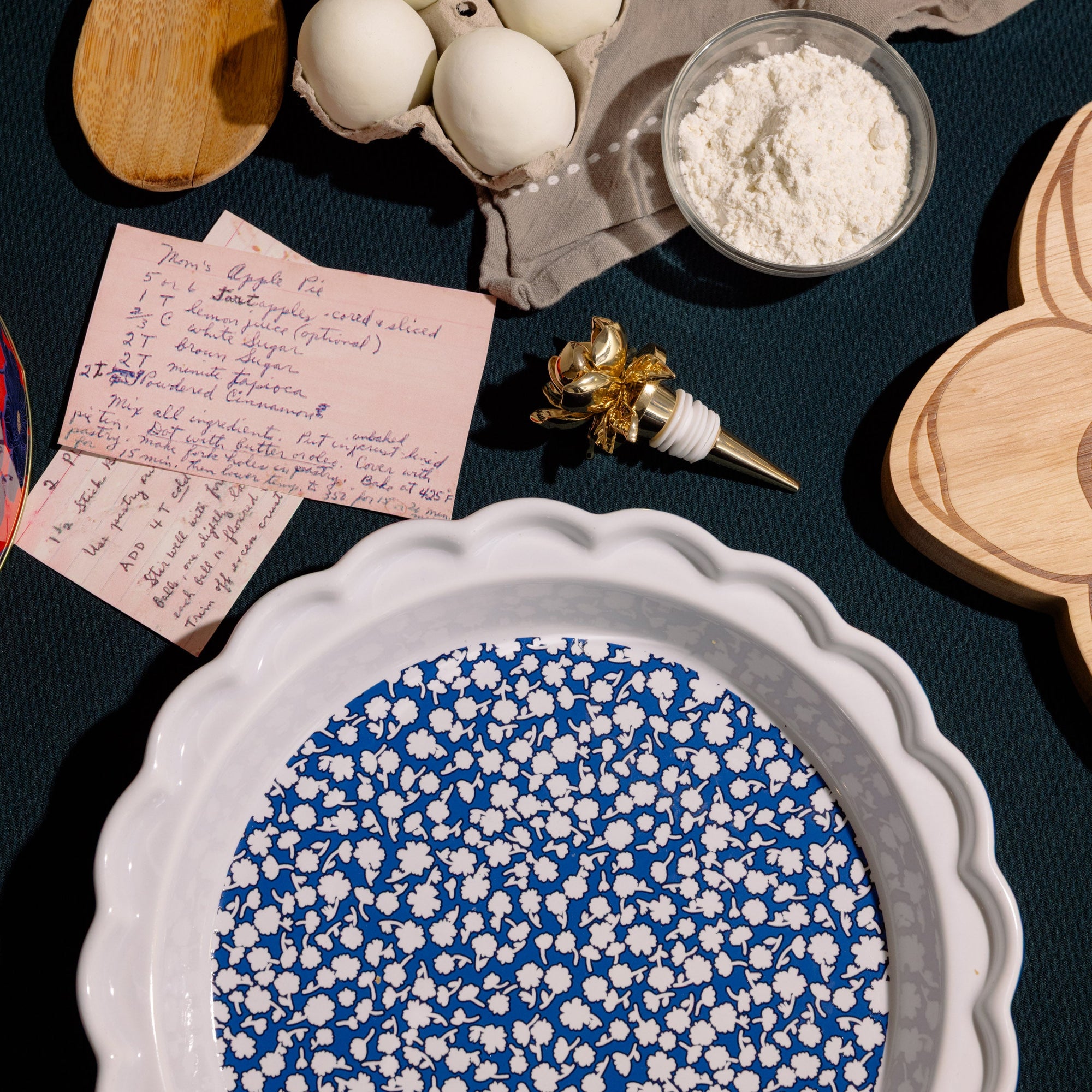 Table with baking items including eggs, flour, a wooden spoon, and a recipe card.