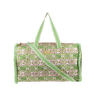 A cylindrical duffel bag with a pink and green circular pattern, featuring light green handles and strap, gold-tone hardware, and fringed edges on a white background.
