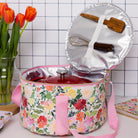 Floral-patterned insulated food container with kitchen utensils on a tiled wall background