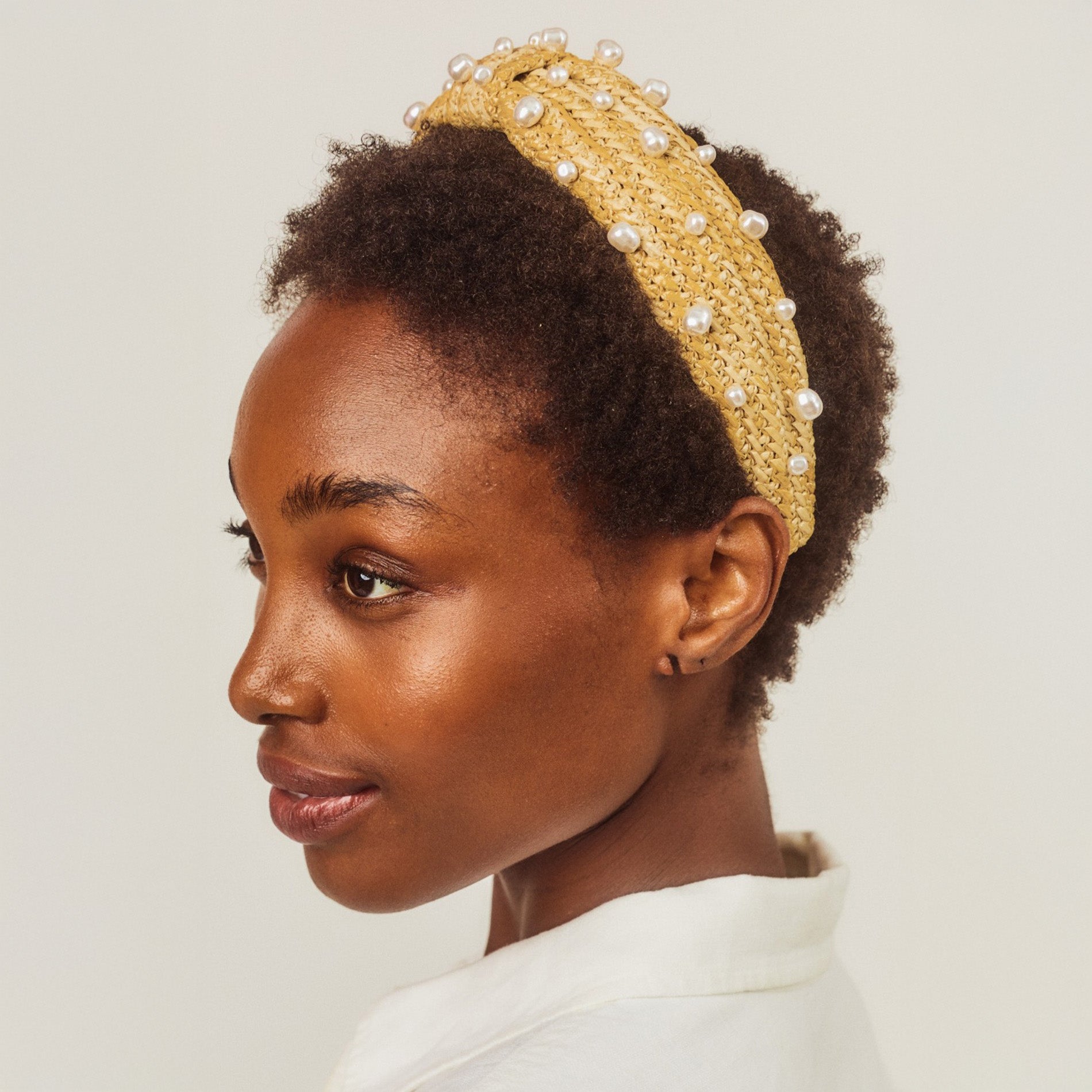 Woman wearing a raffia headband with pearls on a plain background