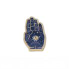 A hand enamel pin with a gold-tone metal border and a dark blue background decorated with gold celestial patterns, stars, and a central eye motif.