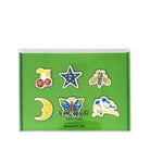 Kate Spade New York enamel pin set in a green presentation box, featuring six pins: cherries, a star, a bee, a crescent moon, a butterfly, and a bird.