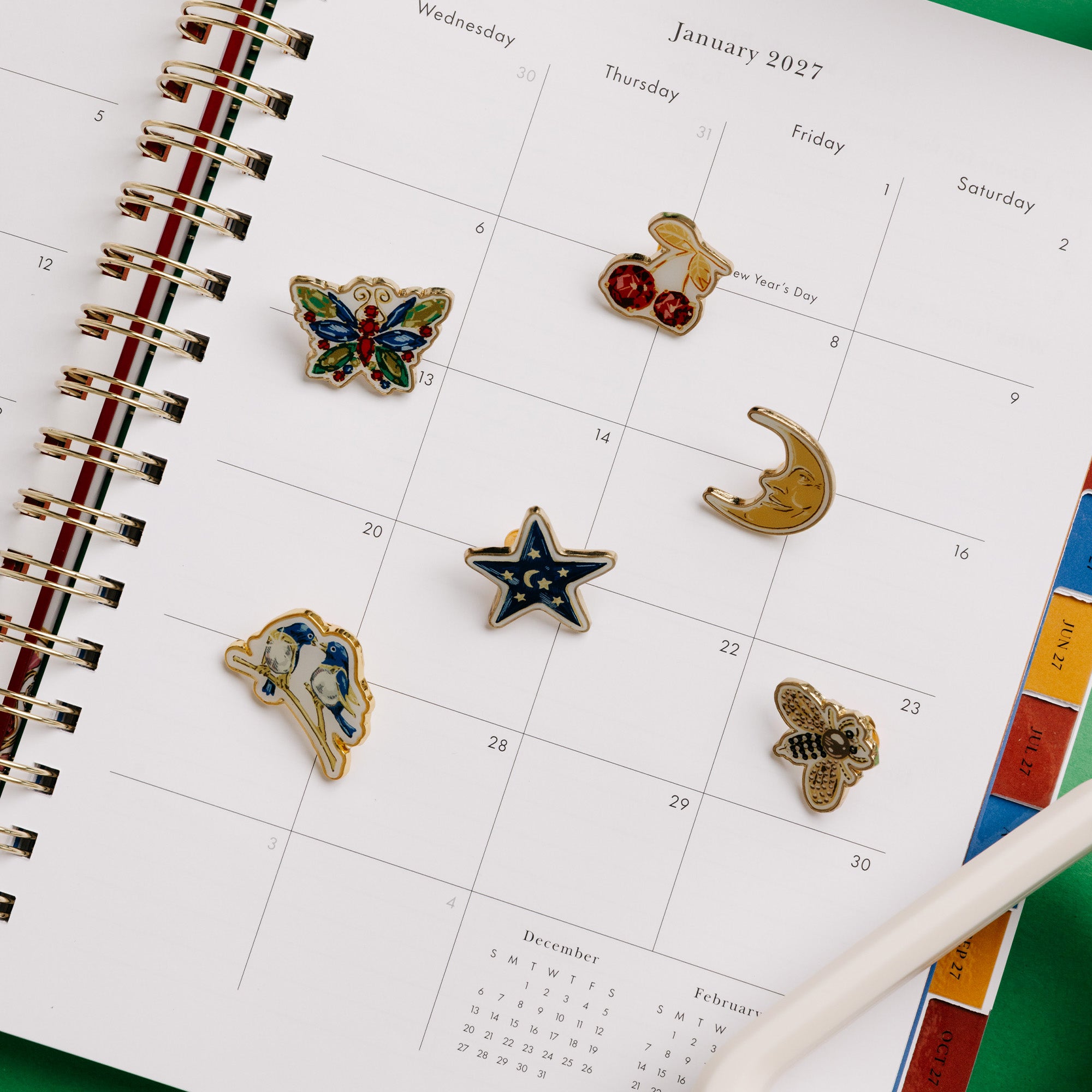 Kate Spade New York enamel pin set in a green presentation box, featuring six pins: cherries, a star, a bee, a crescent moon, a butterfly, and a bird on a planner