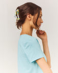 Woman wearing a light blue top against a plain background with a colorful hair claw