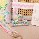 Floral-patterned strap with a gold clasp on a textured surface, with a wicker basket and floral fabric in the background.
