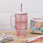 Pink striped mug with straw, floral pouch, and hair accessories on a wooden surface.