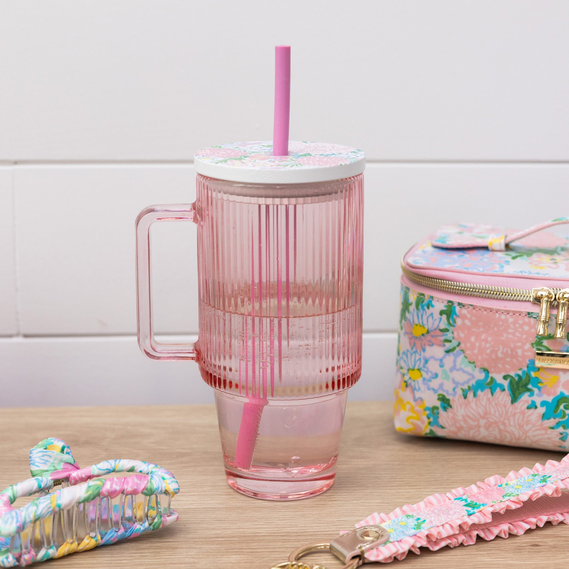 Pink striped mug with straw, floral pouch, and hair accessories on a wooden surface.