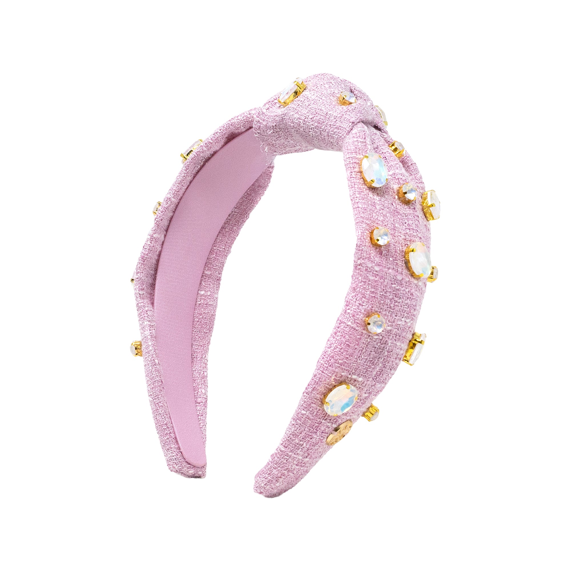 A light pink textured fabric headband with a twisted knot design, decorated with gold-tone metal settings and iridescent rhinestones, shown on a plain white background.