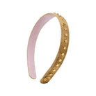 A curved tan leather headband decorated with gold-tone studs and a small gold medallion, featuring a light pink interior lining, shown on a plain white background.