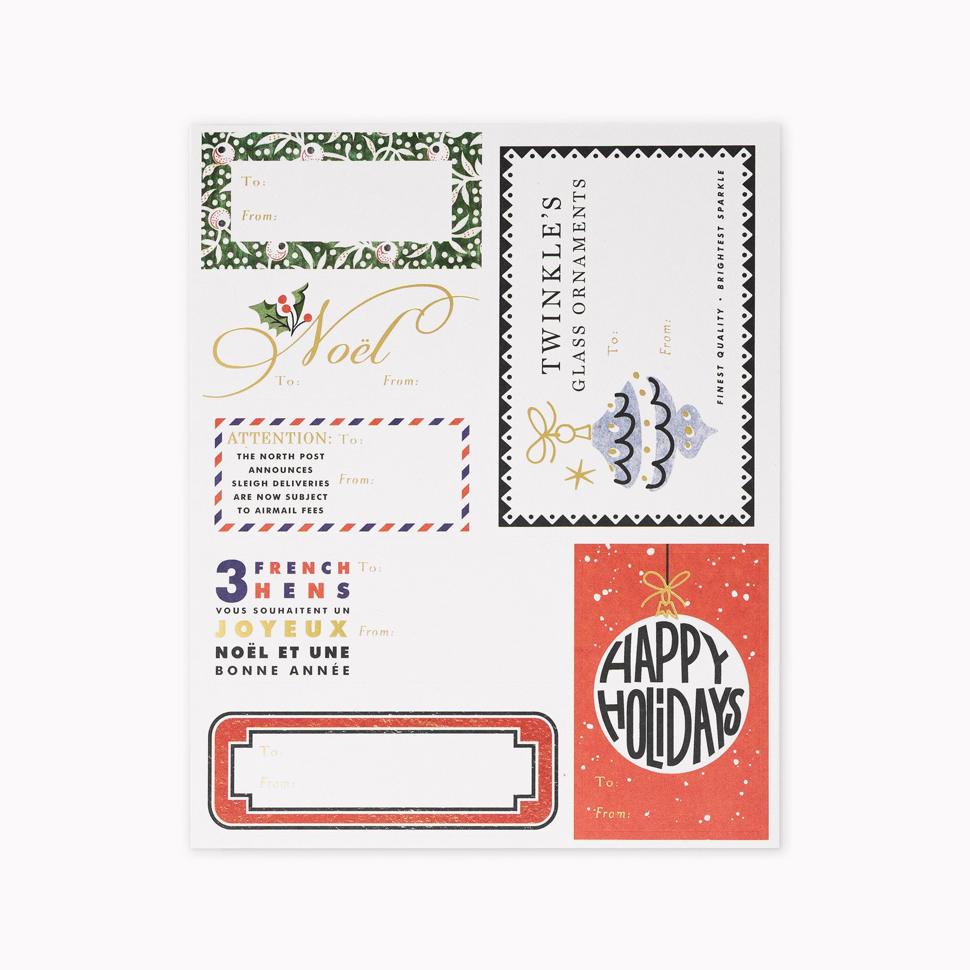 A flat lay of six vintage-style holiday stationery cards and envelopes on a white background. The designs include green holly-patterned frames, gold cursive 'Voilà' text, a black-and-white postage stamp motif with a blue ornament, a red-and-orange French greeting card, and a red 'Happy Holidays' card with gold stars.