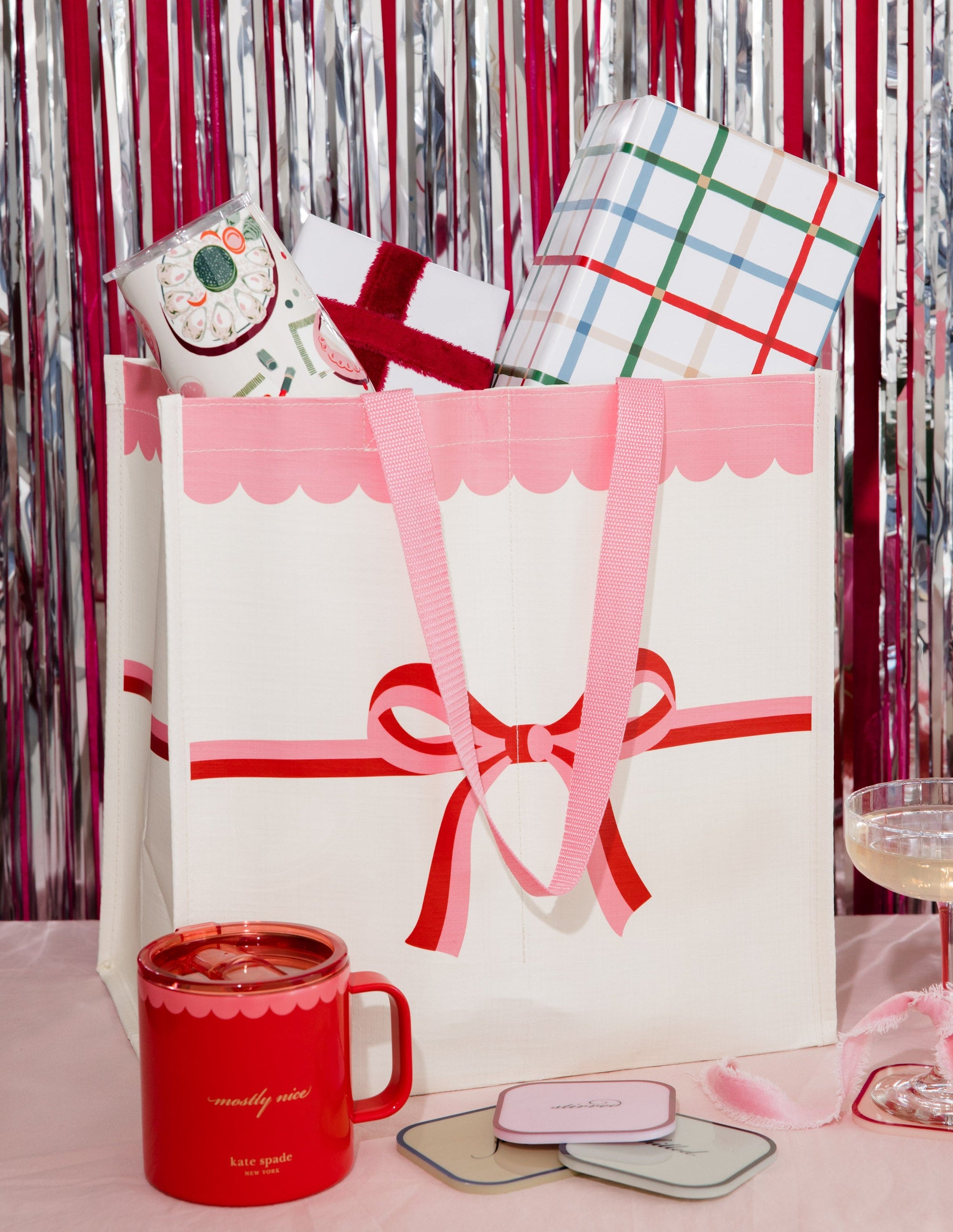 Large gift bag with a pink bow, surrounded by smaller wrapped gifts and a red mug on a festive background.