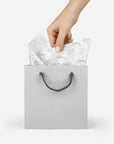 Model pulling silver floral patterned tissue paper out of a silver bag