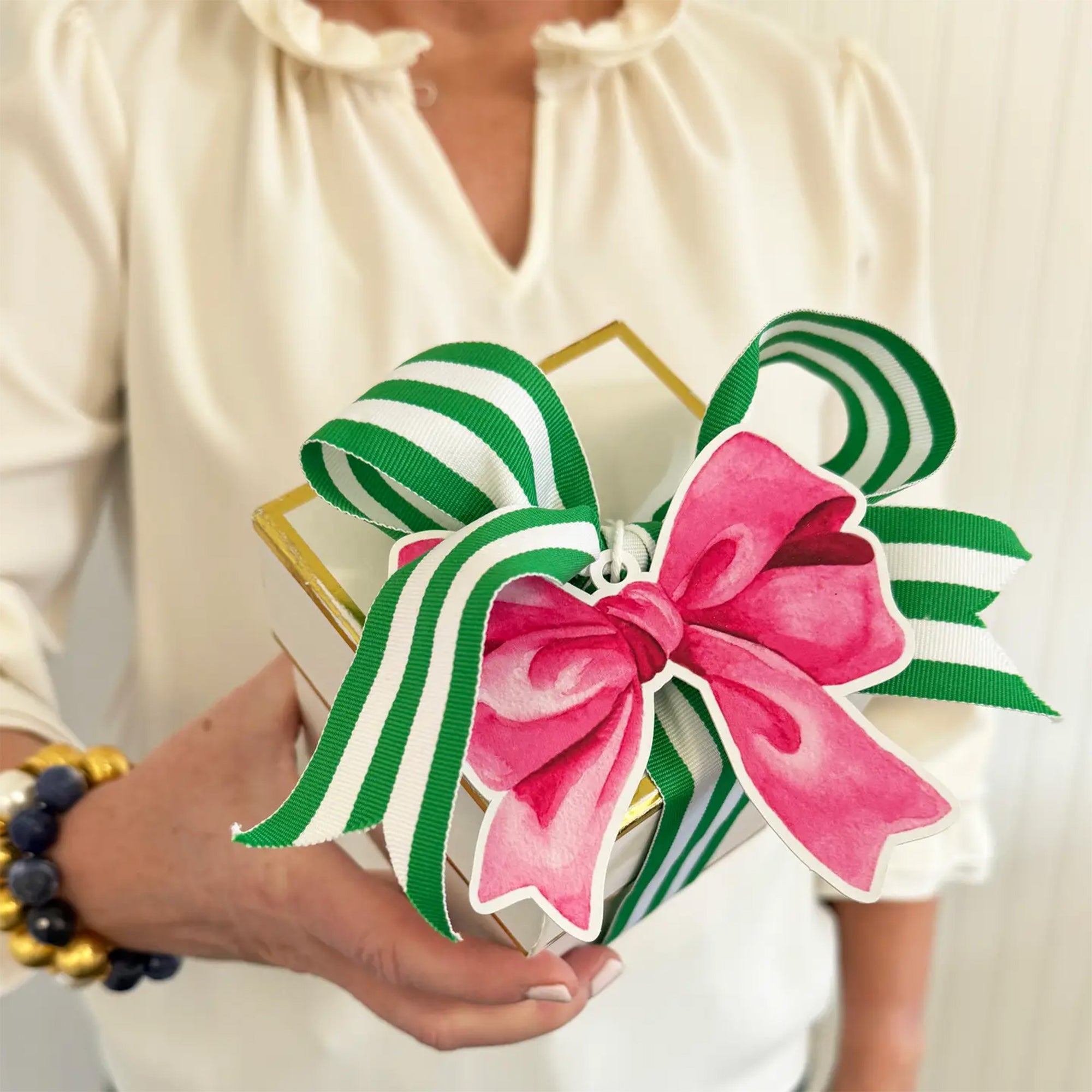 Decorative bow with pink center and green and white stripes held by a person wearing a white blouse.
