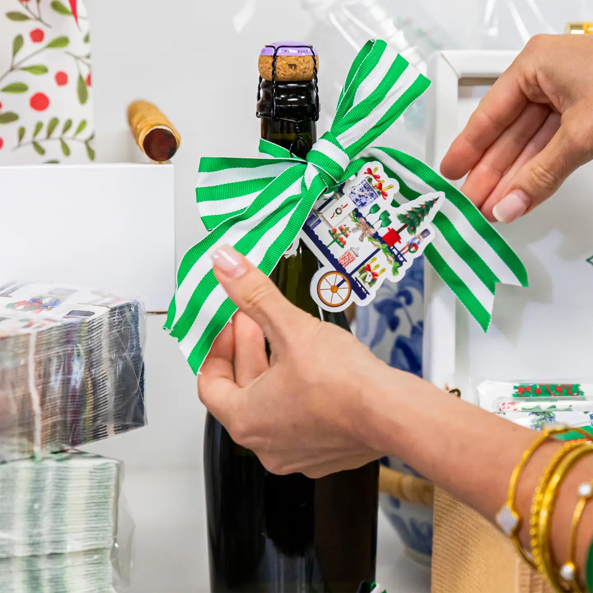 Person wrapping a bottle with a green and white striped ribbon and decorative label.