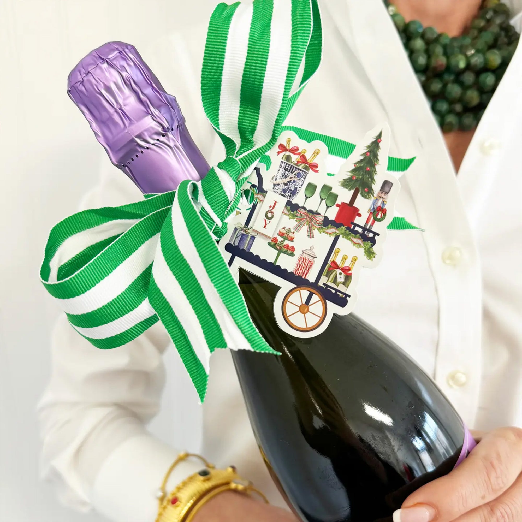 Bottle of champagne with a decorative ribbon and tag held by a person.